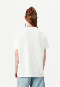 T-shirt bianca in cotone con maniche corte, collo rotondo e vestibilità rilassata, mostrata di spalle su uno sfondo bianco uniforme.