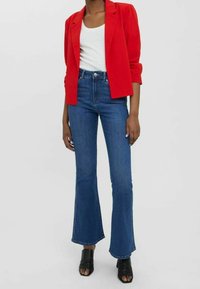 Punainen bleiseri, valkoinen paita, levenevät siniset farkut ja mustat avoimet kärkikorot. Bleiserissä on jämäkkä leikkaus; farkut ovat korkeavyöt�äröiset ja farkkukankaiset.