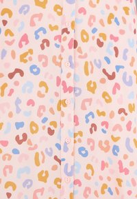 Kevyt, vaaleanpunainen pusero, jossa on leikkisä kuvio abstrakteista muodoista sinisessä, keltaisessa, vaaleanpunaisessa ja ruskeassa. Keskellä napit.