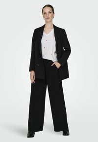 Blazer oversize noir, t-shirt blanc à col en V avec des pois rouges, et pantalon noir à jambe large. Textures lisses et design minimaliste.