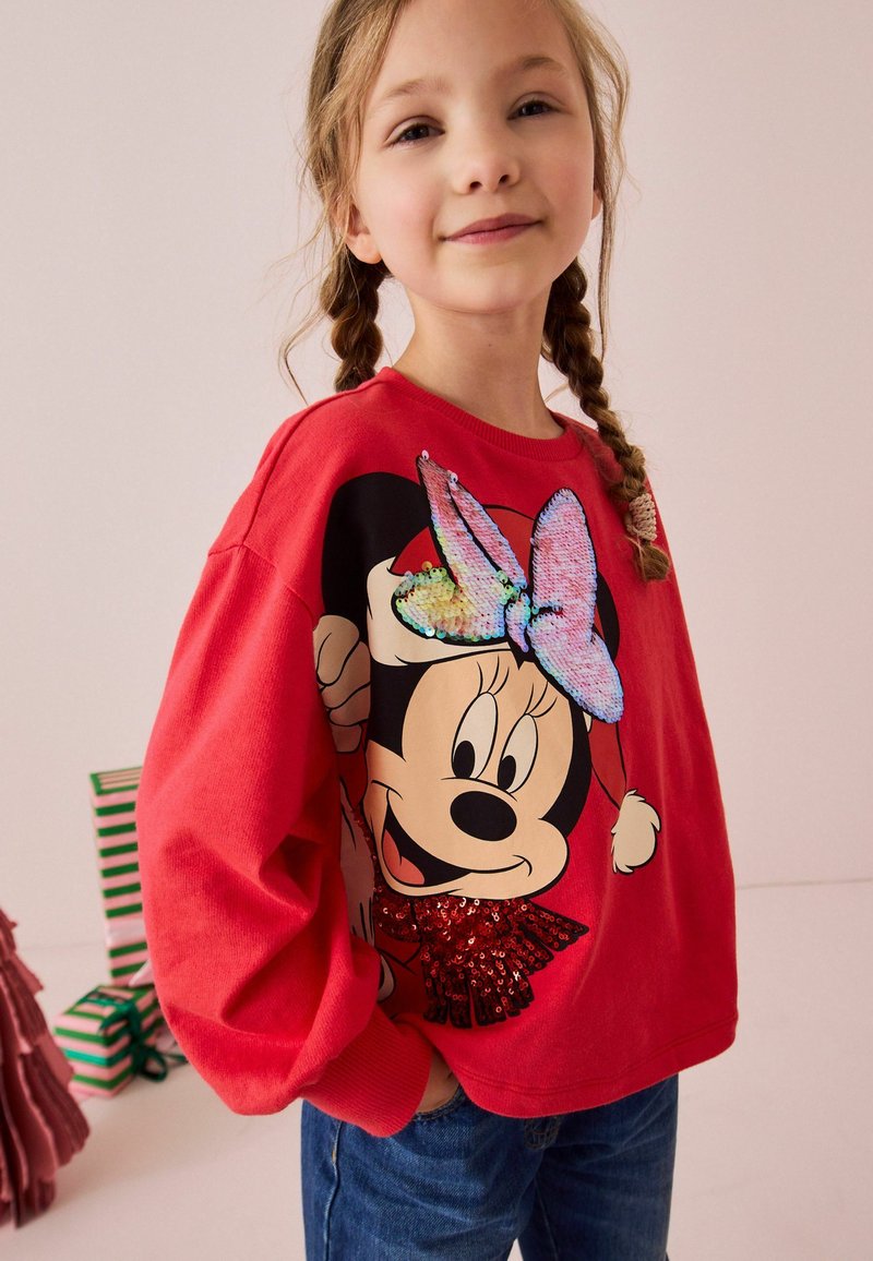 Punane dressipluus, millel on suur Mickey Mouse'i graafika koos sädelevate paelte ja säraaktsentidega, millele on kombineeritud sinised denim teksad.