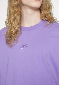 Lila bomull t-shirt med korta ärmar, med en broderad Nike-logotyp i matchande nyans på vänster bröstområde.