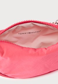 Różowa tkaninowa torba o gładkiej fakturze i zamknięciu na zamek błyskawiczny. Wewnątrz znajduje się jasna podszewka z nadrukiem "TOMMY HILFIGER".