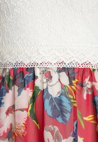 Robe florale avec un corsage en dentelle blanche à détail texturé et une jupe multicolore plissée ornée de grandes fleurs éclatantes.