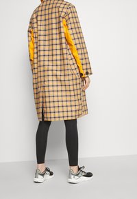 Długi długi płaszcz w żółtym i szarym kolorze, z pomarańczowymi rękawami. Noszony na czarne legginsy i sportowe czarno-białe sneakersy.
