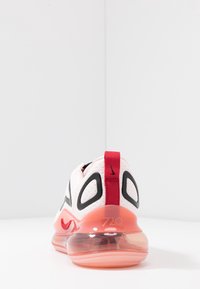 Białe tenisówki z przezroczystą różową podeszwą, czarnymi akcentami i czerwoną pętelką na pięcie. Charakteryzują się perforowaną fakturą i numerem modelu "720."