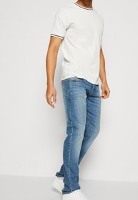 Camiseta blanca de manga corta con cuello a rayas azul marino, combinada con jeans de mezclilla azul claro y zapatillas blancas, mostrando un conjunto casual.