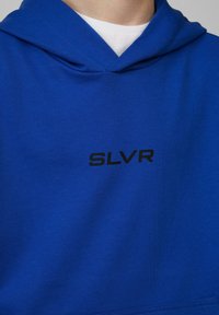 Blauwe hoodie met een zwart "SLVR" logo op de borst. Gemaakt van zachte, gestructureerde stof met een standaard pasvorm en een klassieke capuchonontwerp.