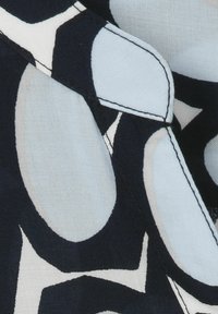 Marineblauer Stoff mit großen hellblauen und weißen abstrakten kreisförmigen Mustern. Glatte Textur mit kontrastierenden schwarzen Nähdetails.
