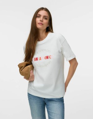 Kobieta o długich brązowych włosach, ubrana w biały t-shirt z tekstem "Santa Monica", trzymająca złożoną brązową kurtkę i niebieskie dżinsy na jednolitym tle.