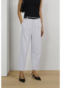 Jasnoszare, lniane spodnie o wysokim stanie z plisami, bocznymi kieszeniami i mankietem, zestawione z czarnym paskiem i czarnymi, spiczastymi szpilkami.