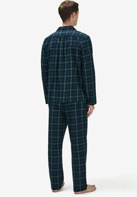 Navyruudullinen yöpuvuntsetti, joka on valmistettu pehmeästä kankaasta. Siinä on napitettava paita ja housut, joissa on joustava vyötärö, vihreät yksityiskohdat.