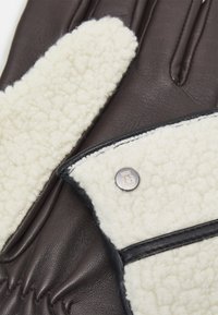 Brown leather gloves featuring a cream shearling panel, black trim, and a silver stud accent near the wrist. Soft texture overall.