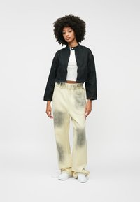 Crna skraćena traper jakna s kopčanjem na dugmad, uparena sa svijetlo bež duksericama s gradijent efektom, nosi se s bijelim tenisicama.