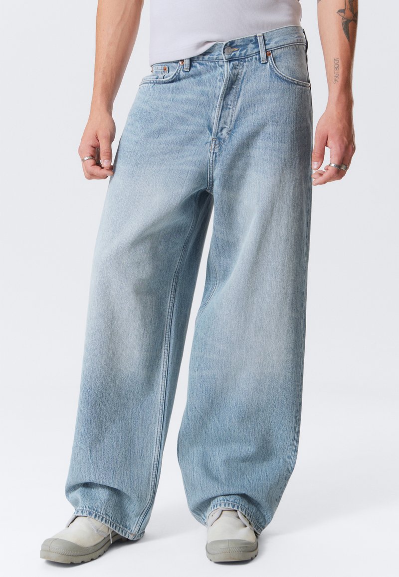 Šviesiai nudažyti, plačiojo kojų džinsai, pagaminti iš denim medžiagos su išblukusiu tekstūru. Penkių kišenių dizainas su mygtukų užsegimu ir kontrastingomis siuvimo siūlėmis.
