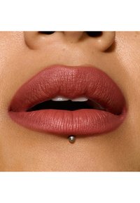 Labbra rosa opache e attenuate con texture visibile e forma piena, caratterizzate da un piccolo perno metallico al centro sotto il labbro inferiore.