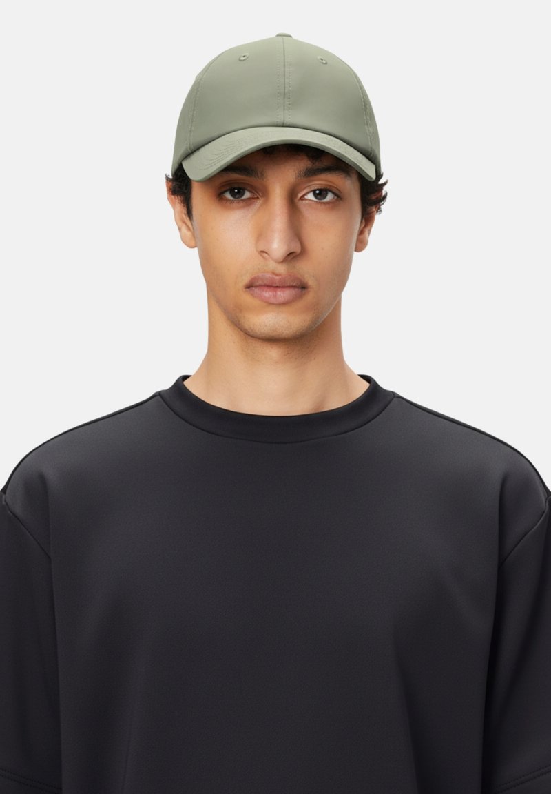 Gorra caqui con una textura suave y diseño de seis paneles, llevada con una sudadera negra de corte holgado. Apariencia minimalista y simplificada.