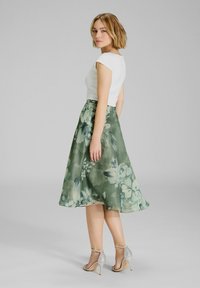 Abito midi A-line floreale con parte superiore bianca aderente, tessuto verde decorato con grandi fiori, completato da sandali con tacco argento.
