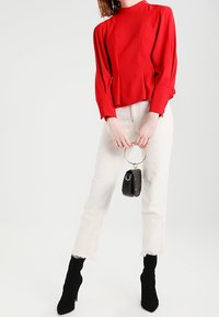 Rød bluse med høj hals og puffede ærmer samt knapdetaljer, kombineret med off-white jeans og sorte ankelstøvler med hæl.