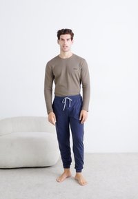 Langermet brun topp og navy joggebukser med elastisk midje og snøring. Teksturet stoff, slim fit, minimallogo.