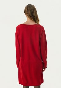 Robe-sweater rouge à manches longues avec une coupe décontractée, un large col et une texture côtelée. L'ourlet tombe juste au-dessus du genou. Design simple et couleur unie.