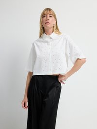 Hvid cropped skjorte med knap-tryk krave og spredte sorte prikker, parret med sorte satinbukser med en glat tekstur.