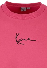 Rosa sweatshirt med ribbad halsringning och en svart broderad logga på framsidan. Tillverkad av mjukt material för komfort.