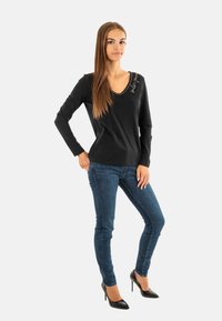Maglietta nera a maniche lunghe con scollatura a V e cuciture decorative, abbinata a jeans skinny in denim scuro e tacchi a spillo neri.