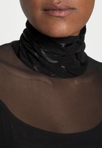 Top a collo alto in rete nera con tessuto leggero, testurizzato e una leggera lucentezza, sovrapposto a un collo trasparente nero. Design morbido e aderente.