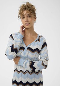 Robe en tricot avec un motif en chevrons bleu, marine et marron, dotée d'un décolleté en V et de poignet froncés. Texture douce et design ajusté.