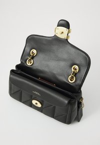 Sac à main en cuir noir avec design matelassé, quincaillerie dorée et accent en chaîne. Il dispose d'une fermeture à fermoir et d'un intérieur rouge.