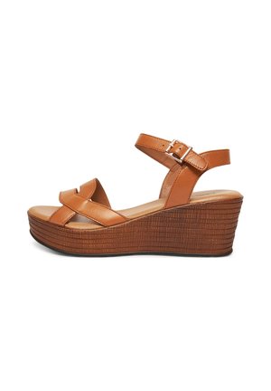 Hnedé kožené sandále na klinovom podpätku majú krížový dizajn, nastaviteľný remienok okolo členku a textúrovanú podrážku. Výška merania je približne 3 palce.