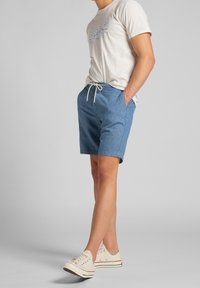 Pantalones cortos de mezclilla azul claros con cintura ajustable, bolsillos laterales y una textura suave. Combinados con una camiseta beige clara que presenta un gráfico azul.