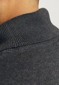 Dunkelgrauer Pullover mit einem gerippten, hohen Kragen. Das Material wirkt weich und strukturiert, mit einem glatten Finish und dezenten Stickdetails.