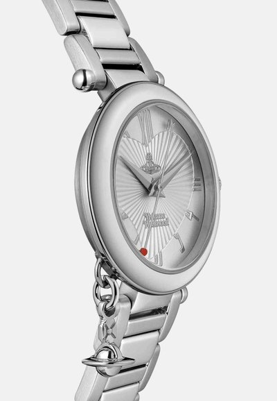 Montre en métal argenté avec un boîtier rond et un cadran texturé effet rayonnement solaire. Elle comporte un accent rouge et un bracelet à maillons réglable.