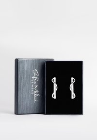 Silverörhängen i loopdesign med kristallaccent, presenterade i en svart sammetsfodrad, blå texturerad låda med en logo på locket.