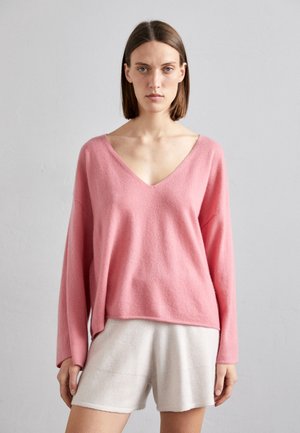 Rosa v-halsgenser med lange ermer og avslappet passform, laget av et mykt stoff. Kombinert med lyse beige shorts, som viser en uformell stil.