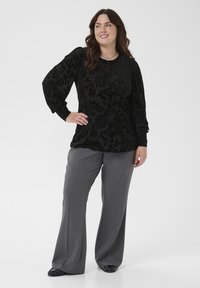Črna bluza s cvetličnim vzorcem in dolgimi nabranimi rokavi. Skombinirana z sivo širokimi hlačami in črnimi čevlji. Preprost, eleganten dizajn.