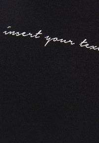T-shirt in cotone nero con ricamo bianco in corsivo che recita "inserisci il tuo testo". Il tessuto ha una trama a costine.