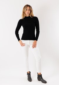 Maglietta nera a maniche lunghe con una vestibilità aderente, abbinata a pantaloni bianchi slim-fit e stivaletti neri alla caviglia con chiusure lampo.