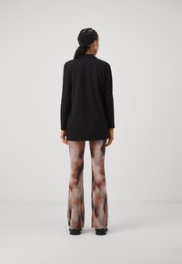 Veste noire à manches longues assortie à un pantalon évasé fluide à motifs avec des nuances de marron et de crème. Texture lisse avec une coupe décontractée.