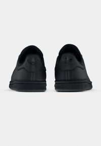 Pár černých tenisek Adidas Stan Smith zobrazených zezadu na světlém pozadí.