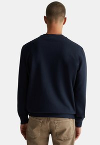 Felpa blu navy con scollo a girocollo e polsini a costine, realizzata in un tessuto testurizzato. Abbinata a pantaloni marrone chiaro.