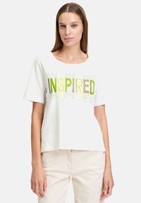 T-shirt en coton blanc à manches courtes et col rond. Présente le mot "INSPIRED" imprimé en lettres vertes et brunes sur le devant.