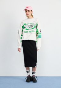 White oversized sweatshirt with green graphics, black ribbed midi skirt with white side stripes, black sneakers, and a pink cap.
