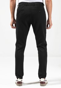Zwarte joggers gemaakt van elastische stof, met een getailleerde tailleband, twee achterzakken en een taps toelopend ontwerp van de pijpen.