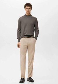 Szary sweter z długim rękawem, beżowe spodnie i czarne mokasyny. Gładka tkanina, luźny krój i subtelna faktura. Minimalistyczny design, bez wzorów.