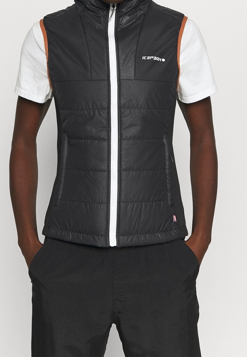 Svart pufferväst med hög krage, vit dragkedja och orange detaljer; har quiltad textur och sidofickor.