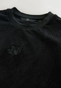 Schwarzer gerippter Pullover mit rundem Ausschnitt, aus strukturiertem Material und einem geprägten Logodetail auf der Vorderseite.