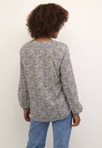 Schwarze und weiße gemusterte Bluse mit langen Ärmeln, Rundhalsausschnitt und strukturiertem Design mit Wirbeln und Streifen. Kombiniert mit blauen Jeans.